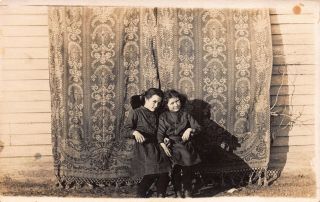 Real Photo Postcard Two Girls Sitting In Front Of Tapestry On House Wall 112390