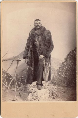 Man In Fur Coat Posed In Front Of Mountainous Backdrop