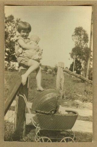 1925 Little Girl Sitting On Fence Post With Doll & Wicker Baby Buggy