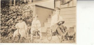 Black And White Photo Of 3 Kids With Tricycles In Front Of Porch