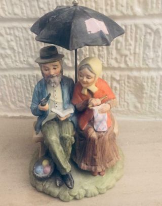 Old Man And Woman Sitting On A Bench Under An Umbrella Figurine